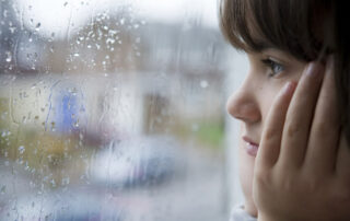 girl looking through a window at the rain