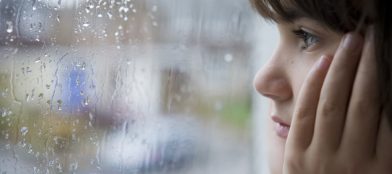 girl looking through a window at the rain