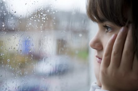 girl looking through a window at the rain