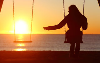 woman sitting alone on a swing at sunset