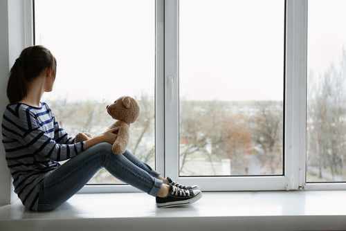 sad girl on a windowsill with her teddy