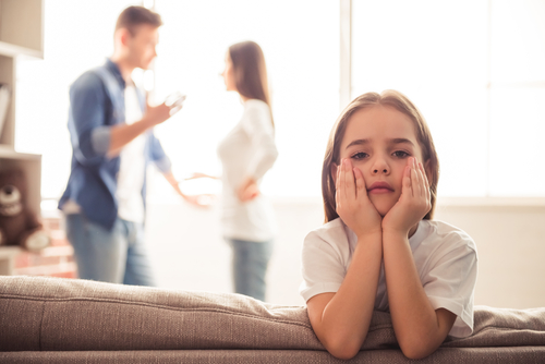 sad little girl with her back to her parents who are arguing